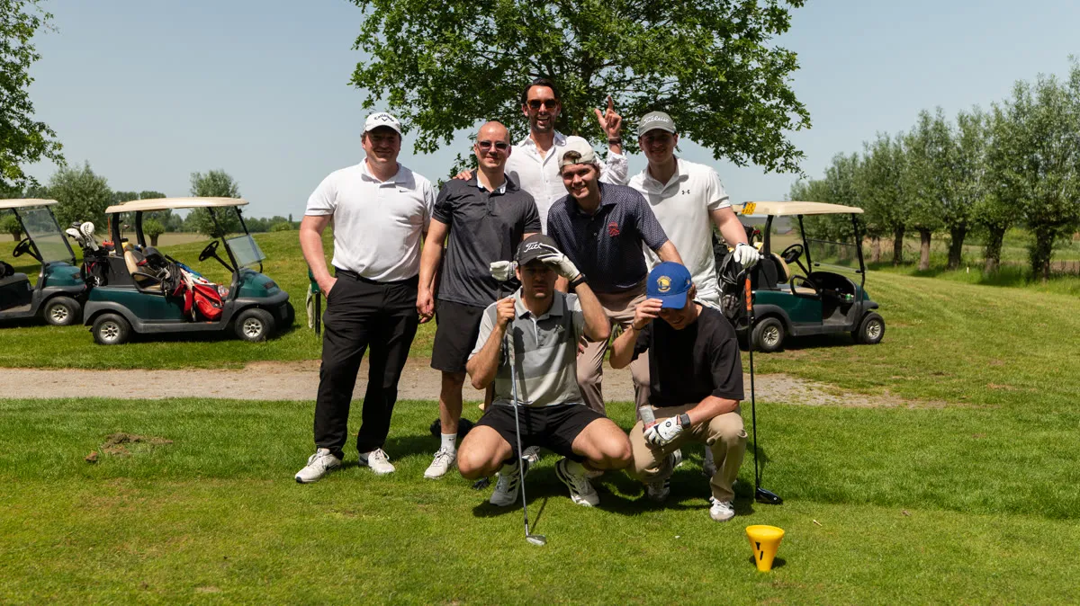 Een team poseert bij de golfkarren, één speler geknield